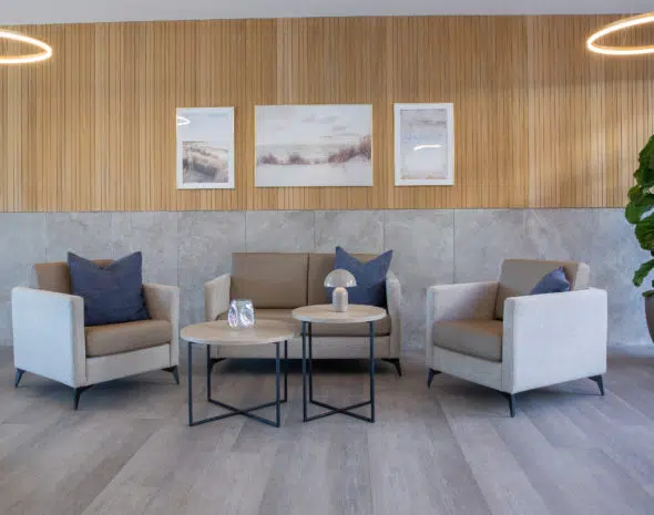 Salon lumineux d’EHPAD aménagé avec fauteuils, canapés et tables basses CARELINE