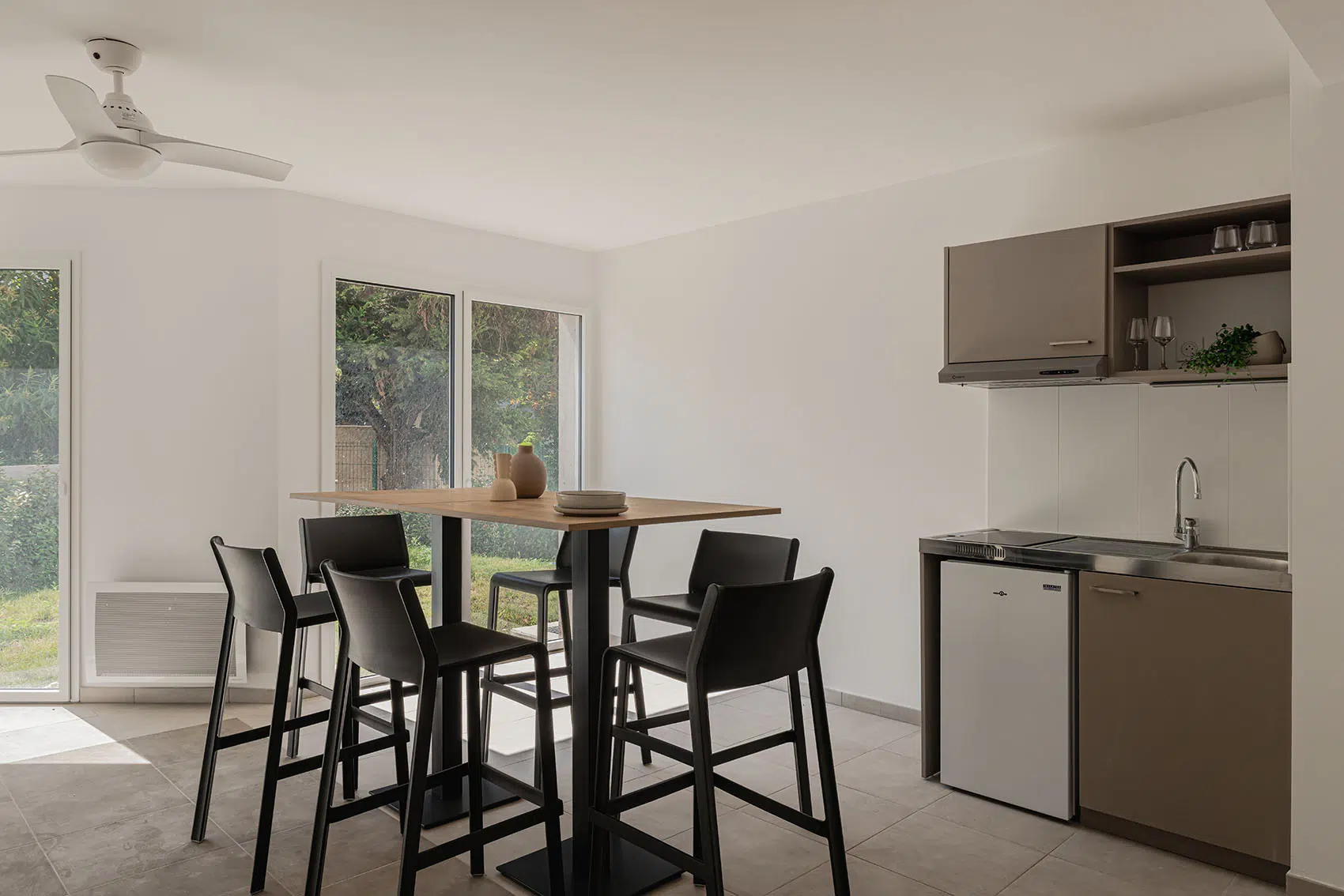Salle commune avec table haute, chaises noires et kitchenette dans la résidence étudiante Le Triangle à Marseille.