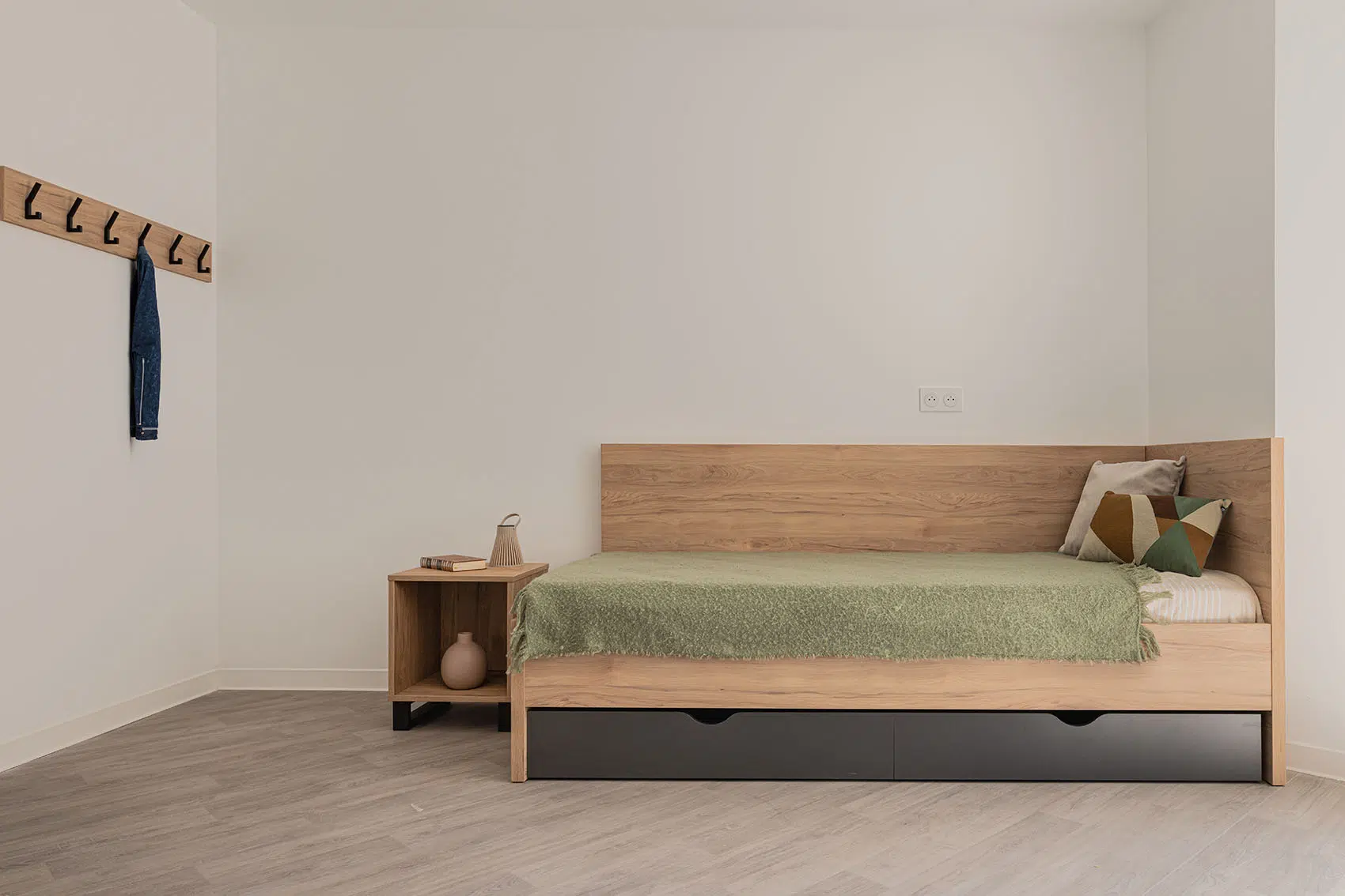 Lit finition bois avec deux tiroirs de rangement et chevet assorti dans un logement étudiant.
