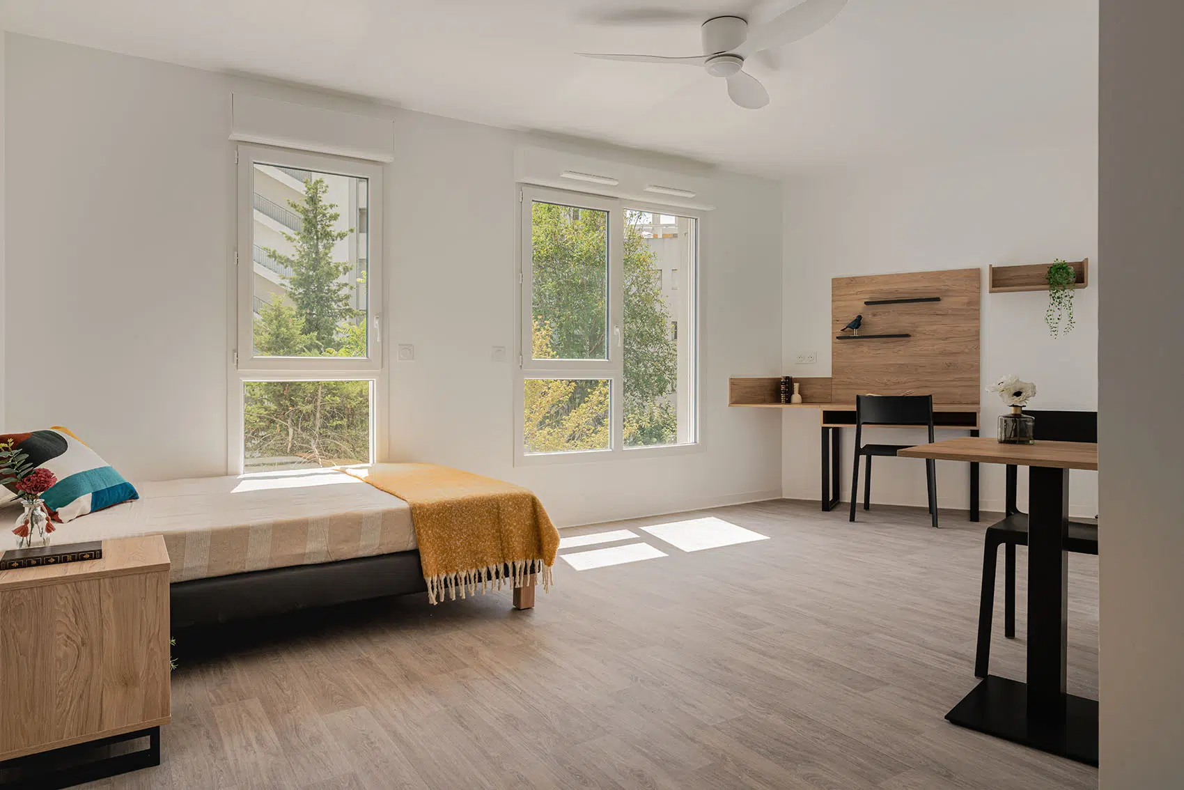 Appartement étudiant lumineux avec lit double, bureau sur mesure, étagères murales et table.