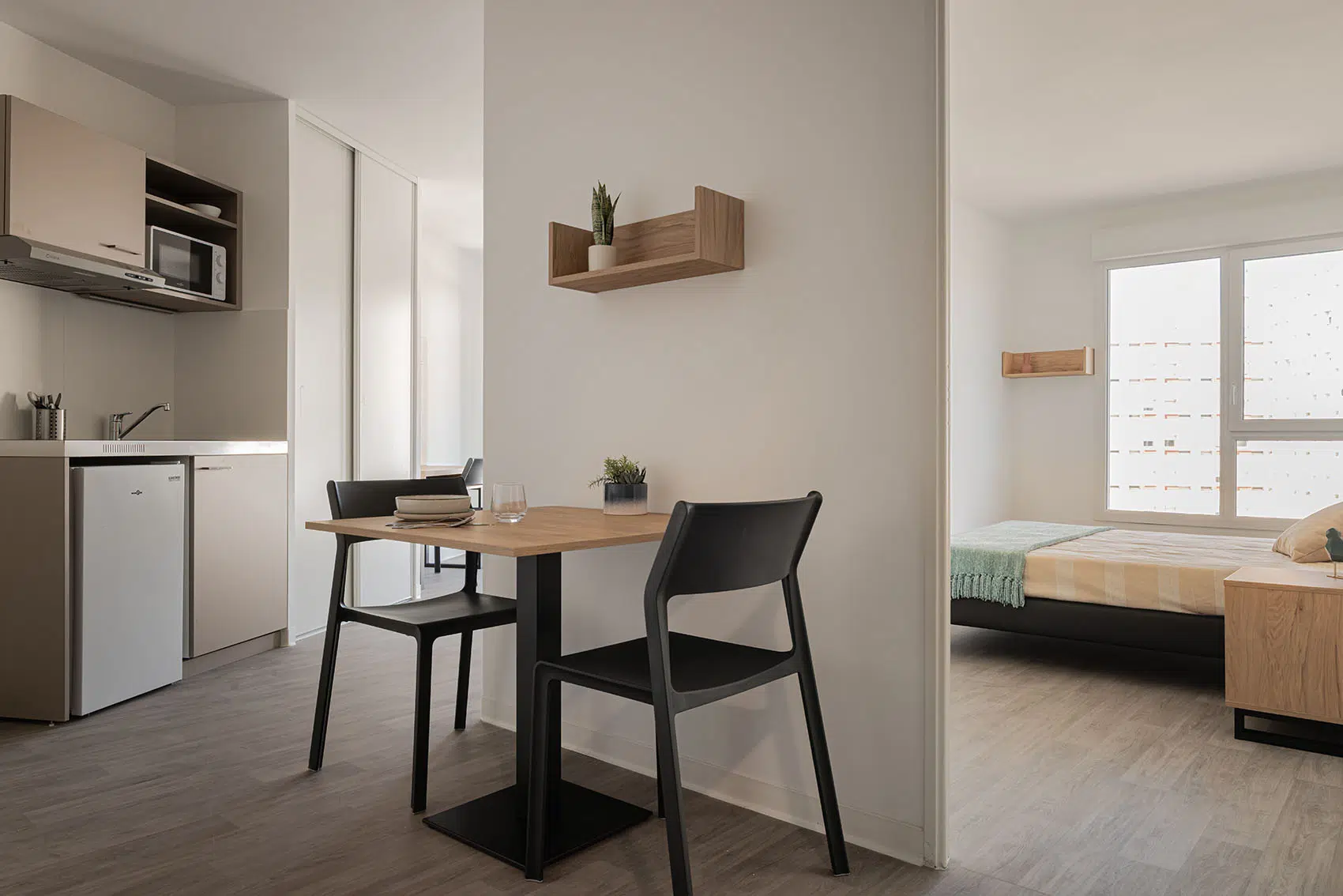 Coin repas avec table carrée et deux chaises noires, à proximité de la kitchenette et de la chambre séparée.