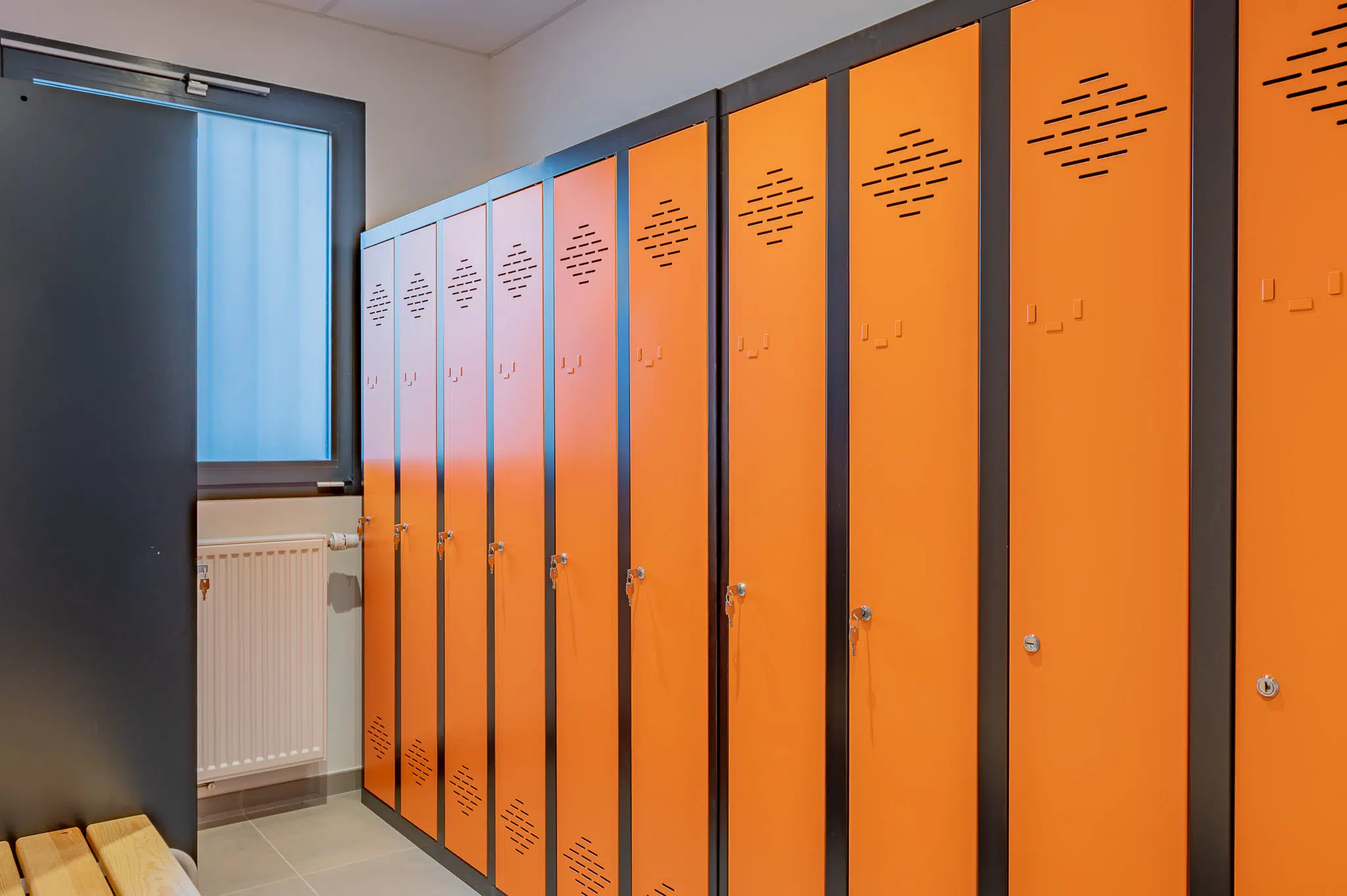 Vestiaires en métal avec façades oranges et banc en bois.