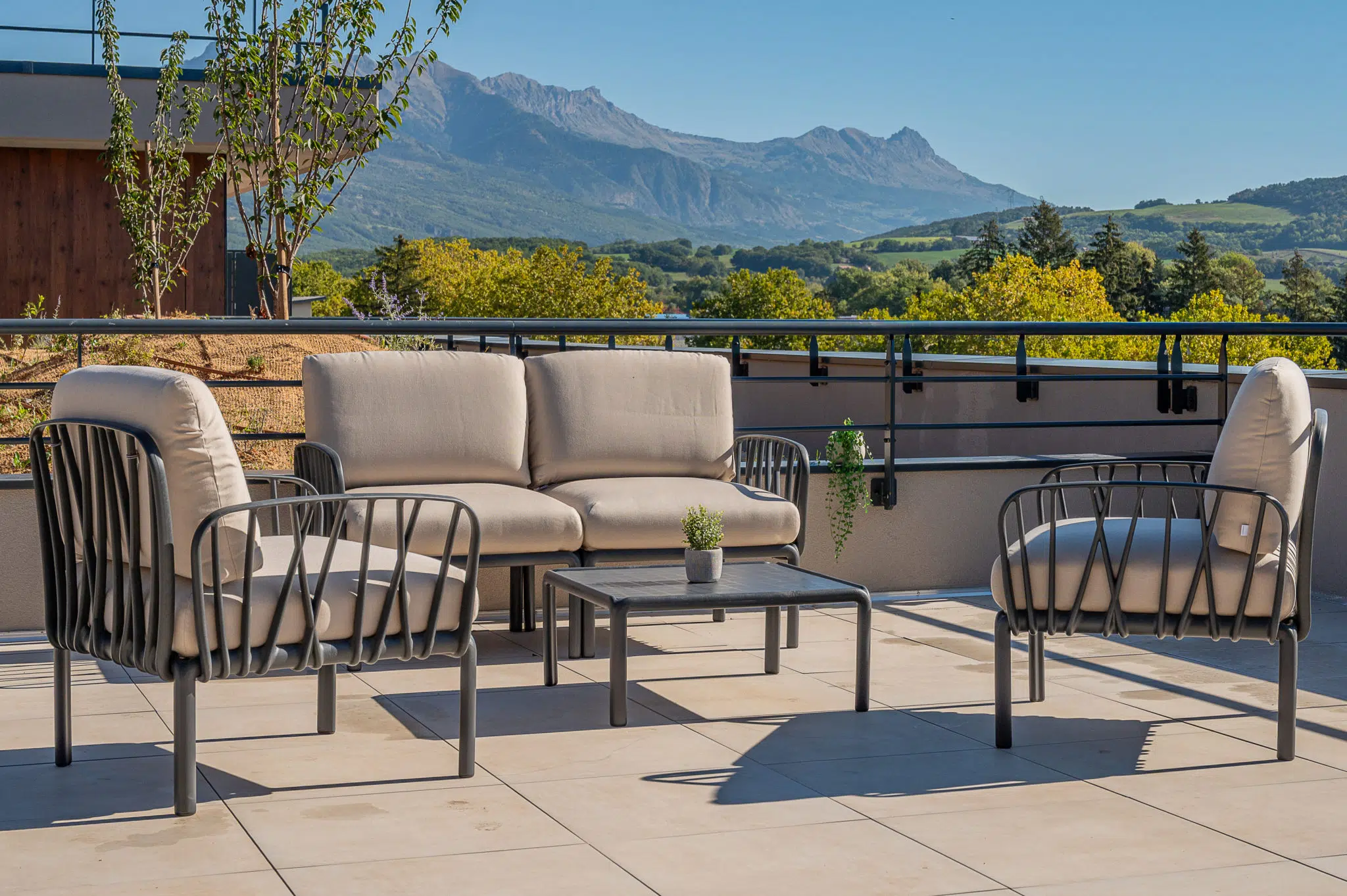 Salon d’extérieur aux coussins clairs sur la terrasse du Bocage à Gap, avec vue sur les montagnes.